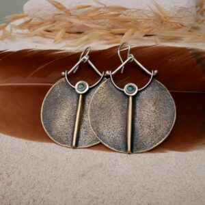 Boucles disque laiton minéral et argent 950 avec tourmaline bleue, posées sur une plume et une bougie — bijou sacré artisanal Bordeaux Eliz'art